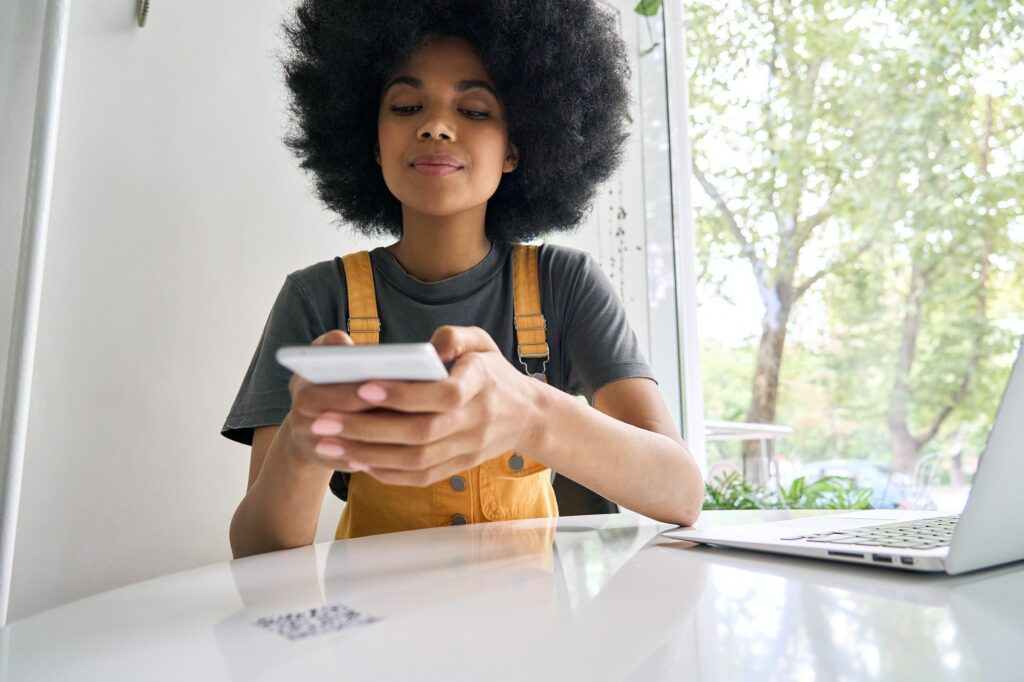 Closeup shot of afro American girl scanning QR code to read menu in cafe.